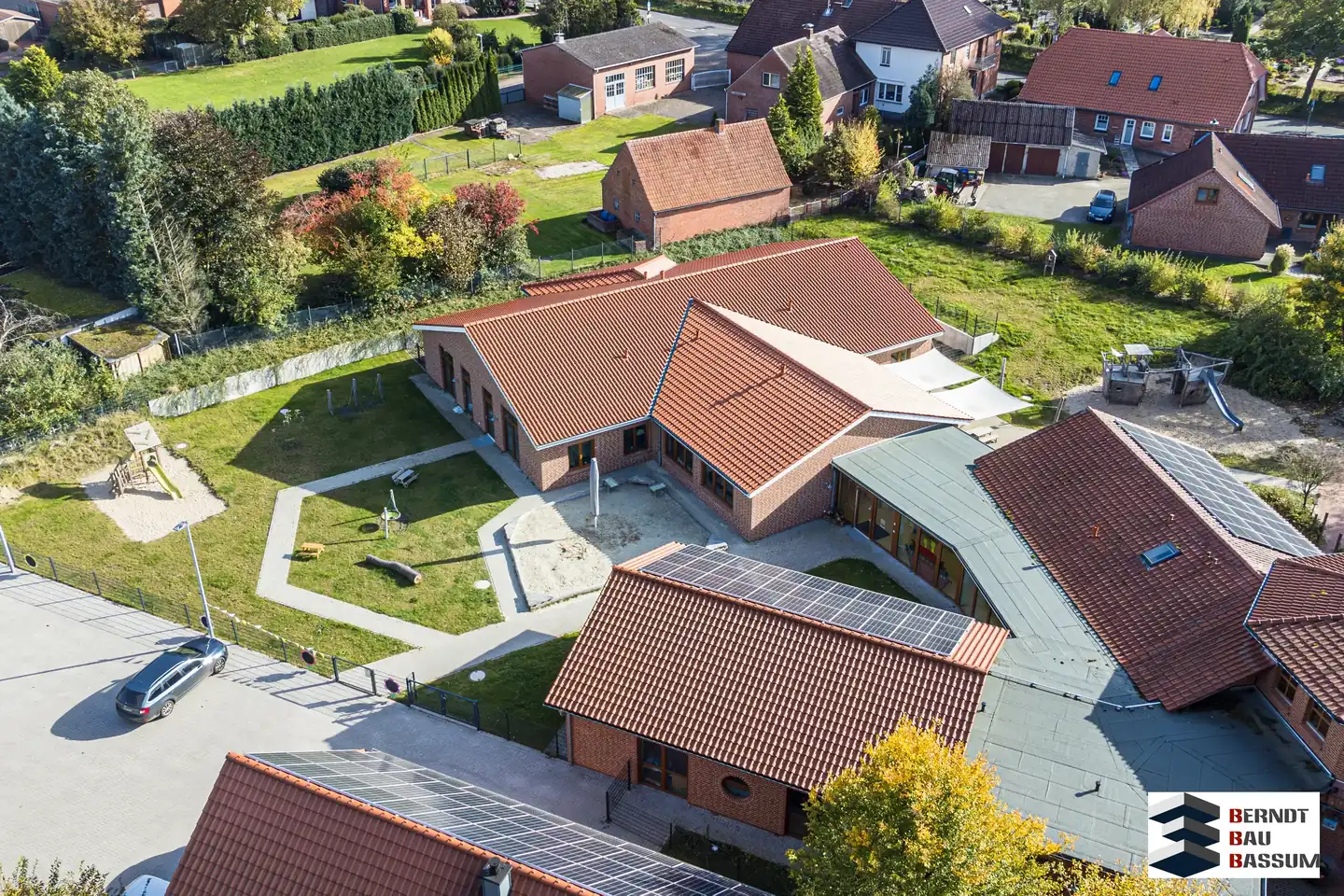 Luftaufnahme eines Neubaus von Berndt Bau Bassum: eingeschossiger Klinkerbau mit roten Ziegeldächern und Solaranlage