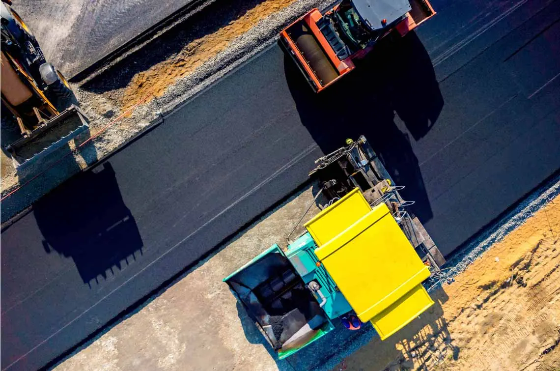 Luftaufnahme: Asphaltfertiger und Walzen beim Einbau einer Deckschicht
